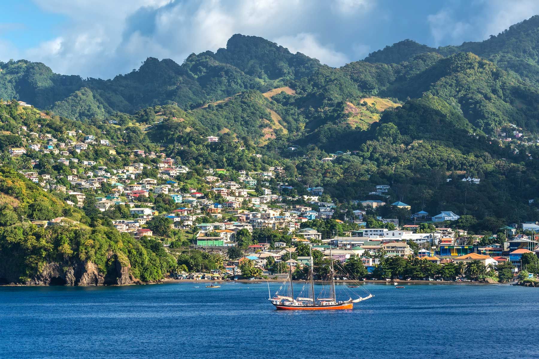 Vista di a costa di u portu è a cità di Kingstown, capitale di l'isula caraibica Saint Vincent. Barca à vela in primu pianu.