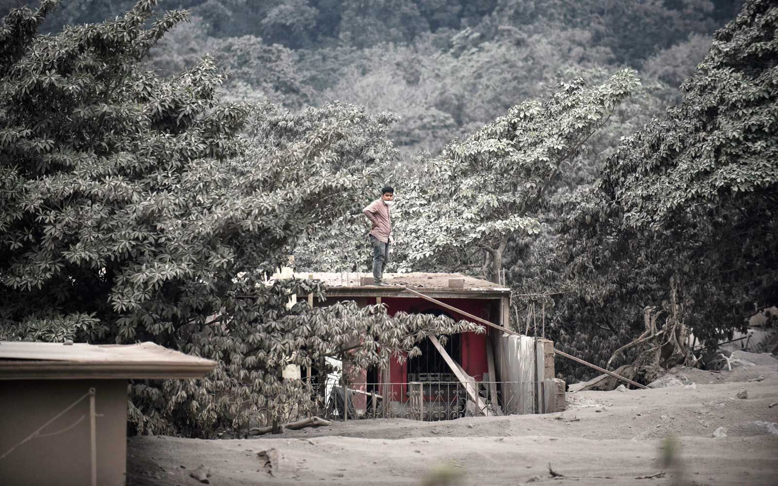 אדם עומד על גג בית בכפר מכוסה האפר סן מיגל לוס לוטס, במחלקת אסקוינטלה, כ- 35 ק'מ דרומית-מערבית לעיר גואטמלה, שנלקח ב -4 ביוני 2018, לאחר התפרצות הר הגעש פואגו.