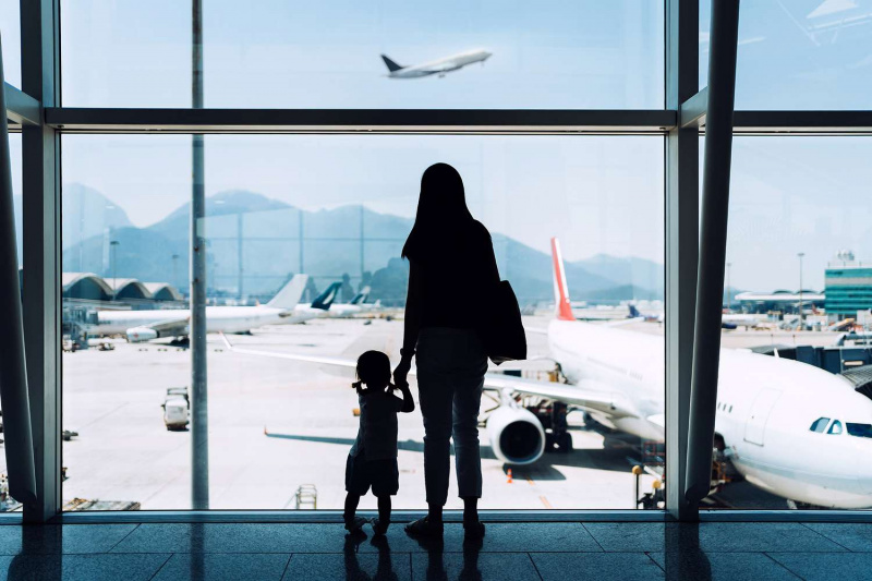   אמא מחזיקה ידיים, בת, מביטה במטוס מבעד לחלון בשדה התעופה בזמן ההמתנה ליציאה