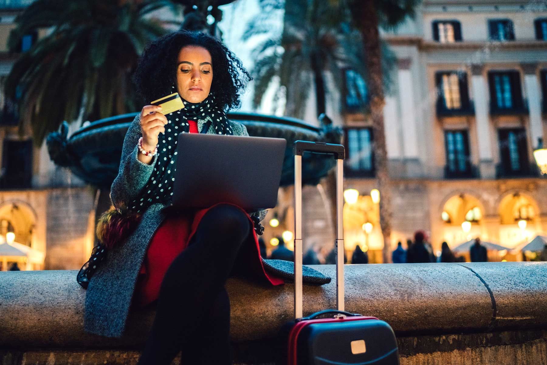 Touristen, die am Brunnen auf der Placa Reial sitzen und mit Kreditkarte eine Online-Reservierung für ein Last-Minute-Hotel vornehmen