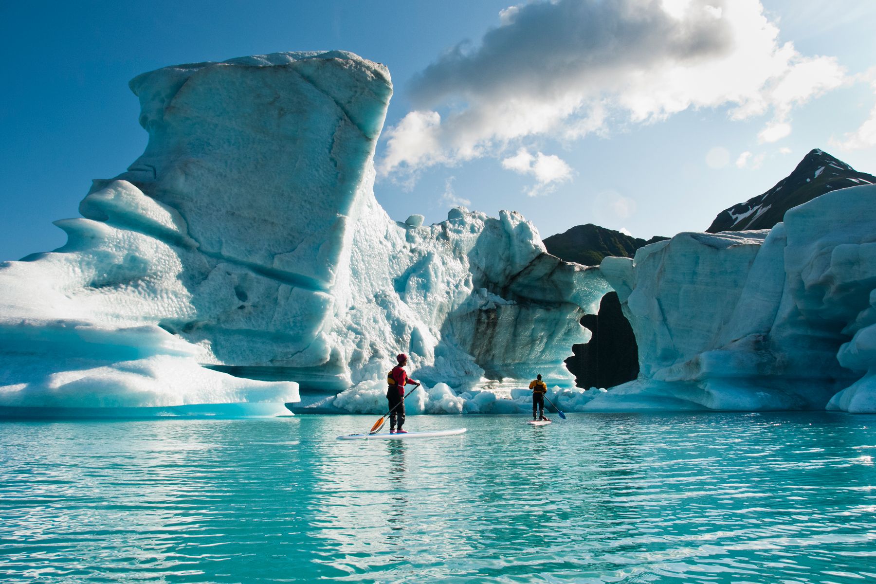 Dui adulti nantu à u stand up paddle board (SUP) osservanu u foru fundutu in l'iceberg nantu à u Lago Bear in u Parcu Naziunale di i Fiordi Kenai, Alaska.