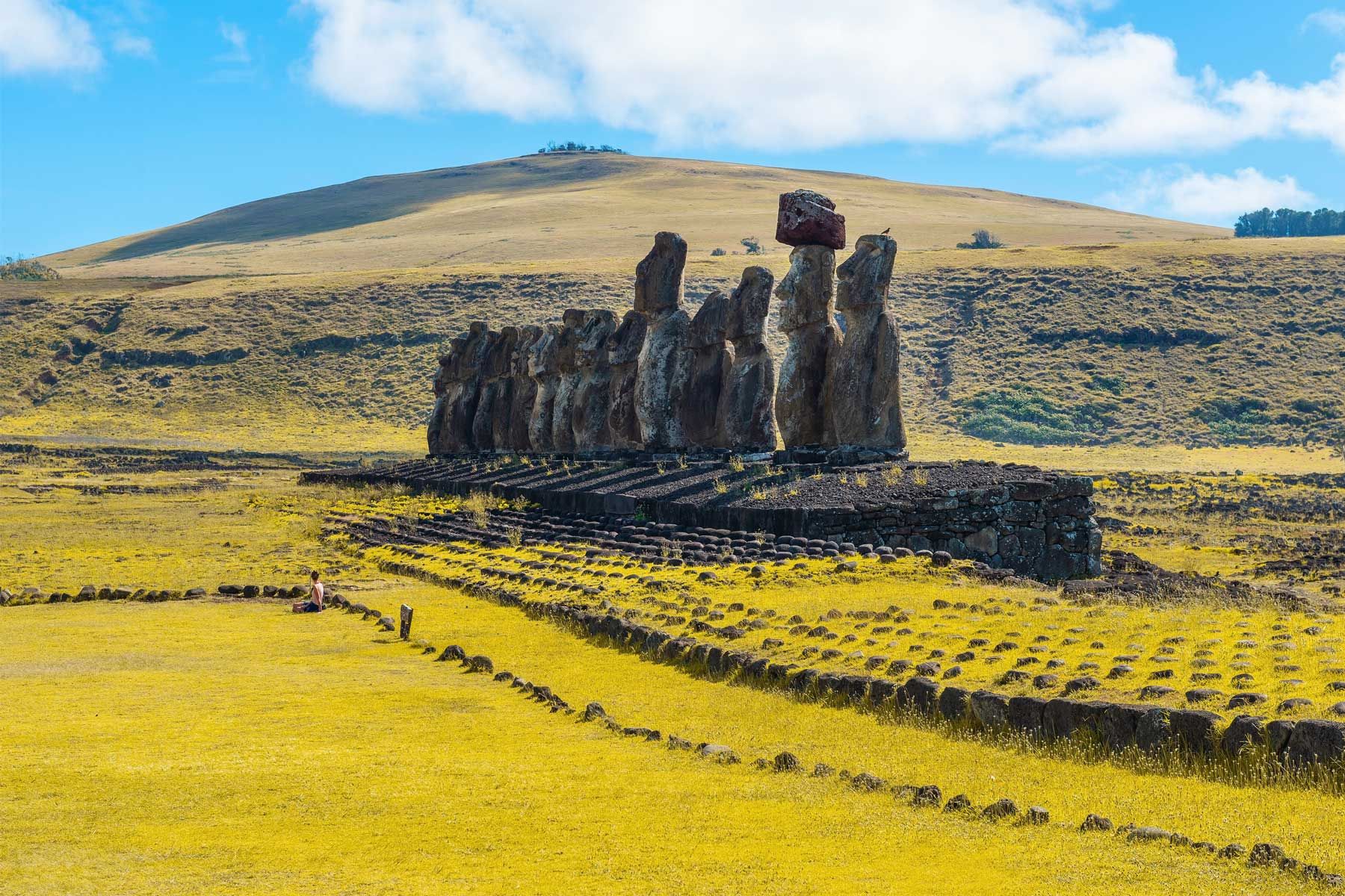 Junge Frau Tourist sitzt vor den Moai-Statuen von Ahu Tongariki, Osterinsel (Rapa Nui), Chile.